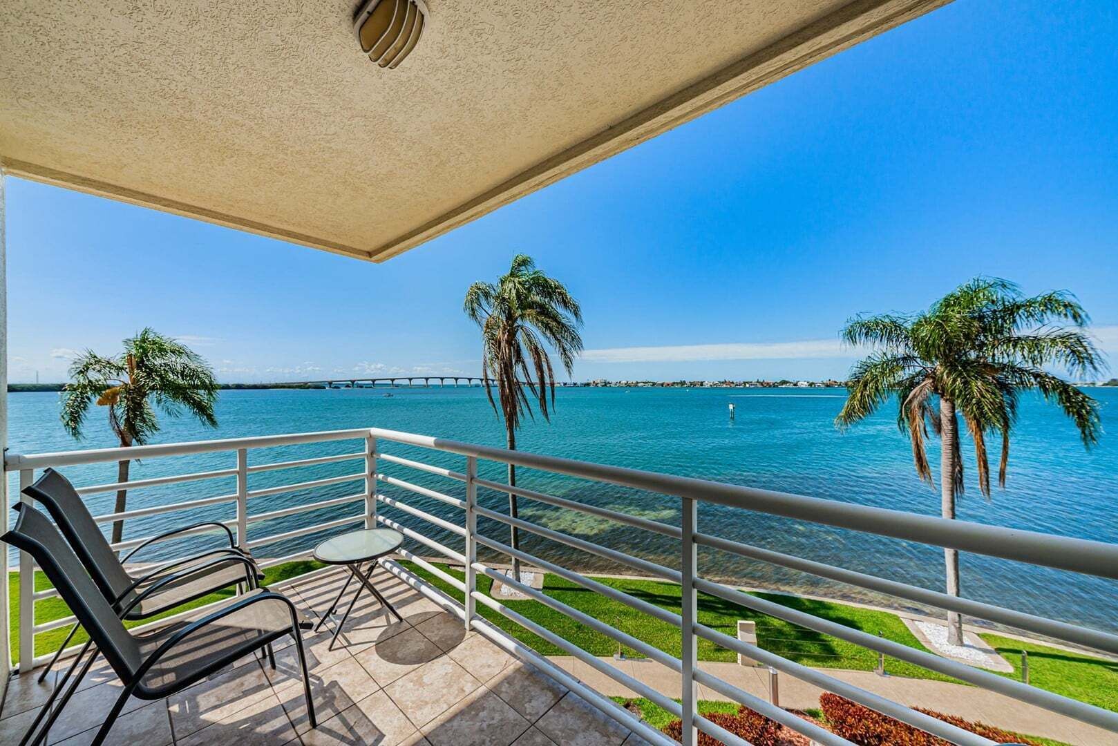 Un balcón con vista al mar, palmeras y un puente distante.