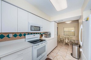 Una cucina compatta con mobili bianchi, un forno a microonde, un fornello, un tostapane e un frigorifero.