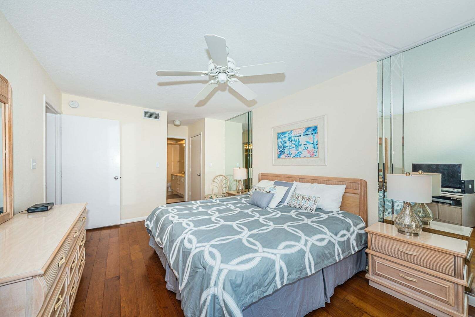 Een slaapkamer met een bed, een dressoir, een spiegel, een plafondventilator en kunst aan de muur.