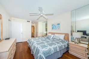 A bedroom with a bed, dresser, mirror, ceiling fan, and artwork on the wall.