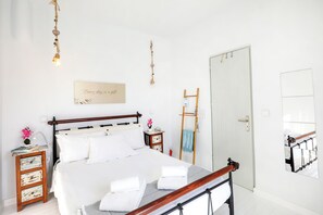 A bedroom with a wooden bed, white bedding, a bedside table with a lamp, a wall-mounted mirror, and a door with a towel rack.