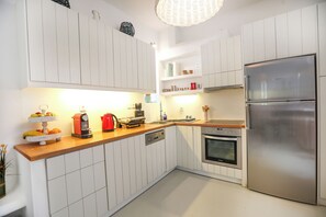 A kitchen with white cabinets, a stainless steel refrigerator, a wooden countertop, and a built-in oven.