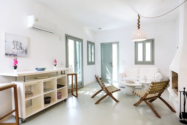 A spacious living area with a white sofa, a wooden chair, a white coffee table, and a white console table with shelves.