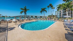 Una piscina con sillas de descanso y sombrillas, rodeada de palmeras y un cielo azul despejado.