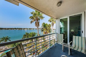 A balcony with a view of the sea, palm trees, and a distant bridge.
