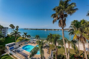 A resort with a swimming pool, palm trees, and a view of the sea.