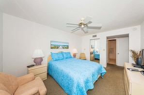 A hotel room with a bed, bedside lamps, a desk with a computer, a chair, and a ceiling fan.