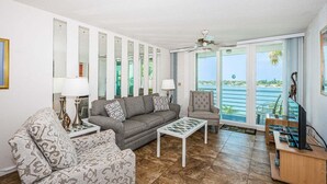 Salón con sofá, sillón y mesa de centro, televisor y balcón con vista al mar.