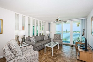 Salón con sofá, sillón y mesa de centro, televisor y balcón con vista al mar.