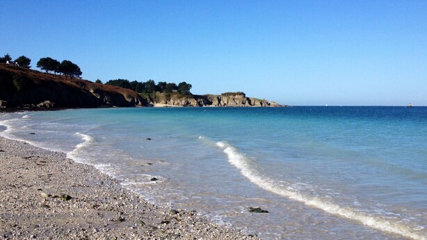 Ein Strand mit Kiesufer, klarem blauen Wasser und steilen Felsen.