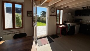 Eine geräumige Küche mit Holzbalken, ein Essbereich mit Tisch und Stühlen sowie ein Blick auf den Garten durch offene Türen.