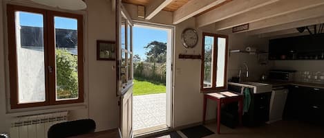 A spacious kitchen with wooden beams, a dining area with a table and chairs, and a view of the garden through open doors.