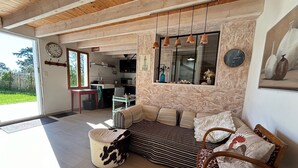 Ein geräumiges Wohnzimmer mit Holzboden, einer Sofagarnitur, einem runden Hocker und einem Essbereich, der durch eine geöffnete Tür sichtbar ist.