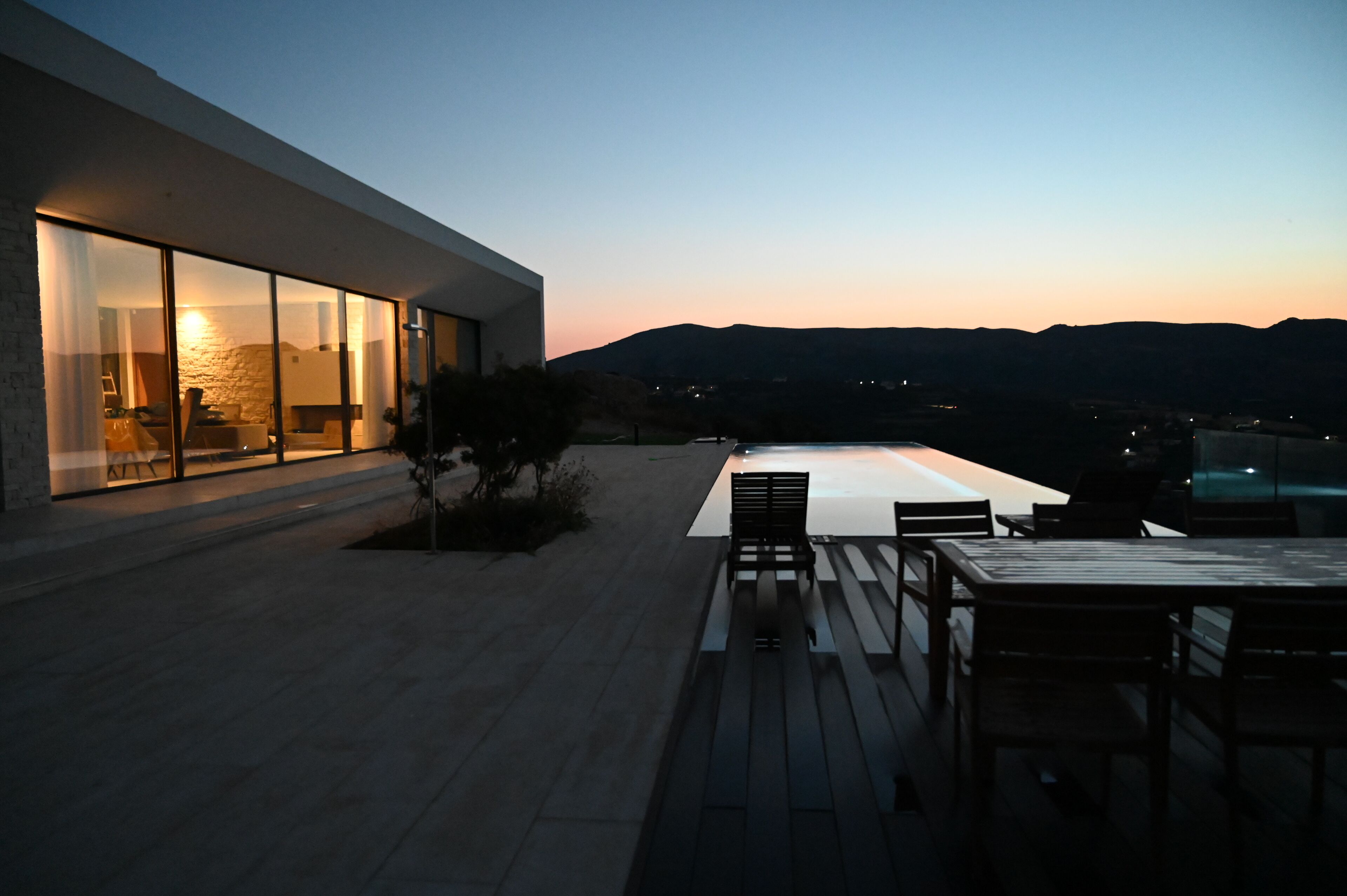 Patio moderno all'aperto con piscina, zona relax e vista sulle montagne al crepuscolo.