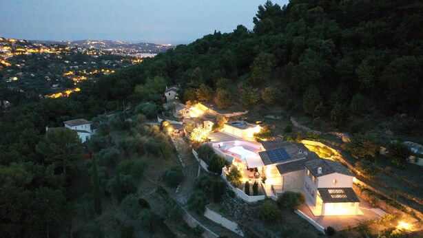 Una proprietà su una collina con diversi edifici, tra cui una casa dotata di pannelli solari sul tetto e una piscina.