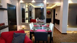 A modern living room with a dining area, featuring a red sofa, a dining table set with plates and cups, and a large mirror reflecting the room. - Elite Residency (Amman)