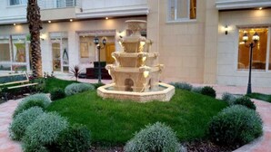 A multi-tiered fountain in a landscaped garden with trimmed hedges and a building in the background. - Elite Residency (Amman)