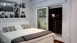 A bedroom with a bed, a large window, and a cityscape view. - Elite Residency (Amman)