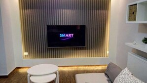 A modern living room with a flat-screen TV mounted on a wall, a white sofa, and a small white table. - Elite Residency (Amman)