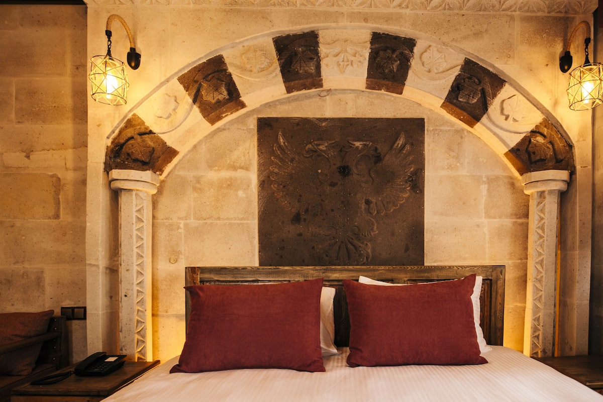A room with a stone fireplace, two red pillows, and a bed with white bedding.
