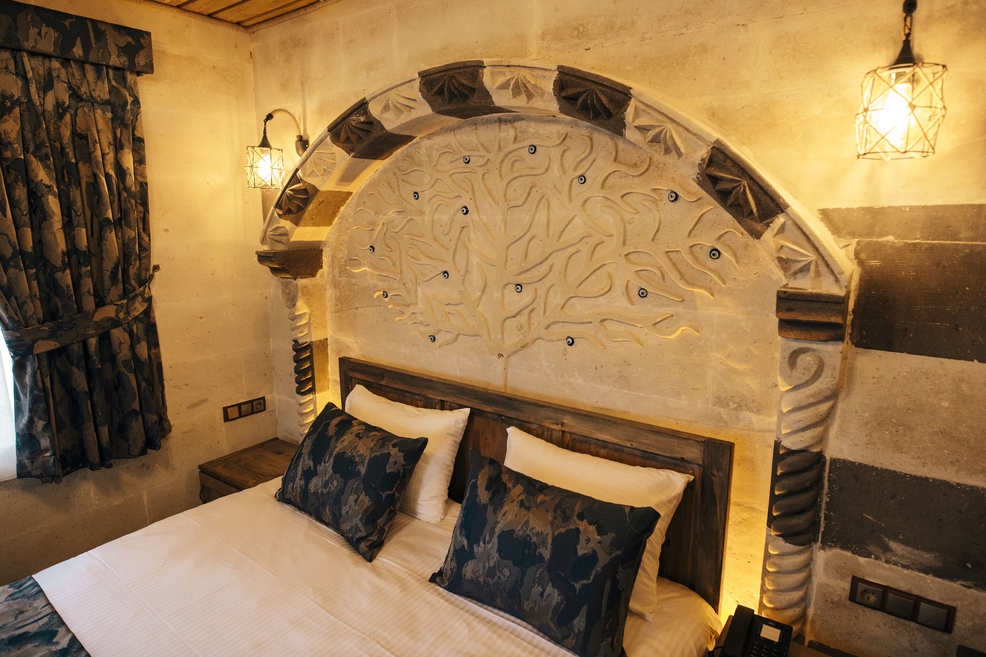 A bedroom with a large bed, a decorative headboard, and two wall-mounted lamps.