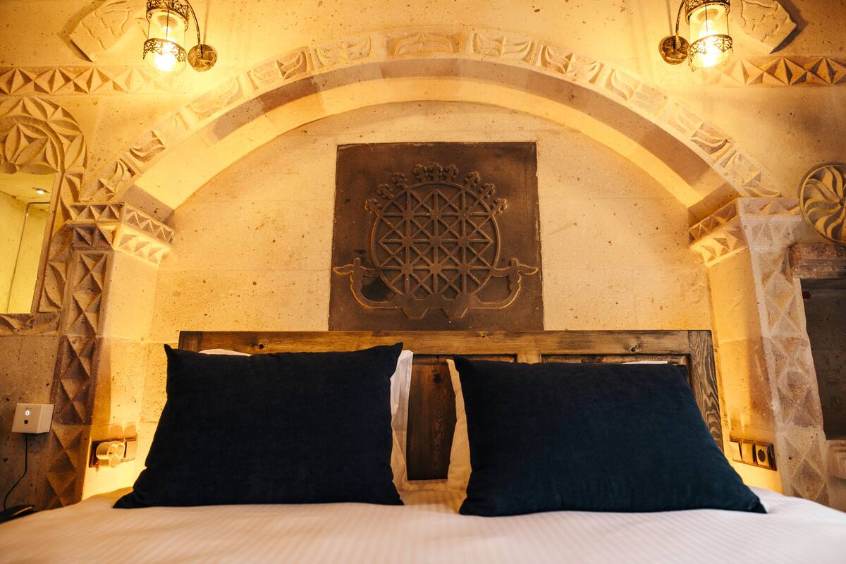 A bed with dark pillows, a wooden headboard, and a decorative wall with a geometric pattern and a central emblem.
