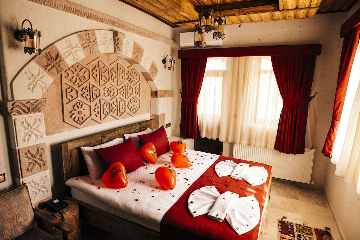 A hotel room with a bed, decorative wall, and red curtains.