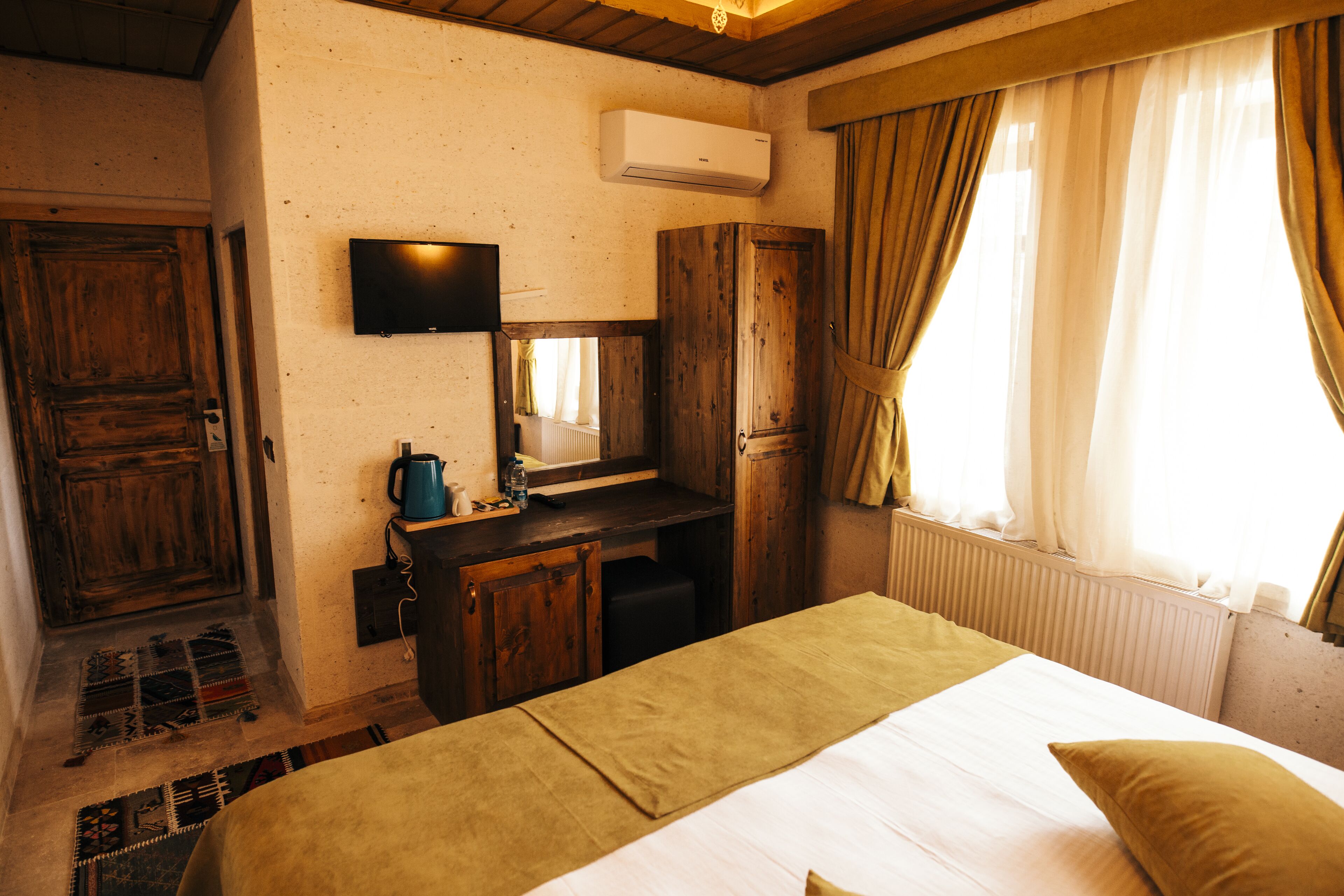 Ein Zimmer mit einem Bett, einem Holztisch, einem Fernseher und einem Fenster mit Vorhängen.