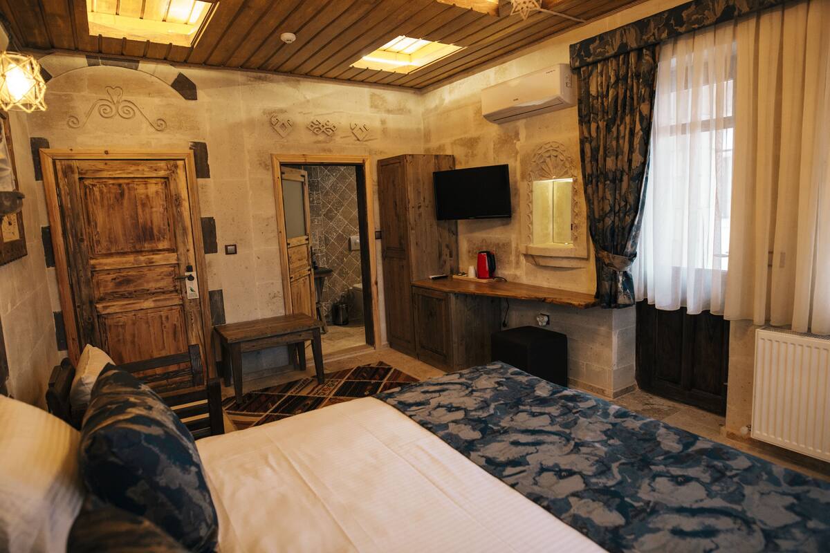 A bedroom with a bed, a desk, a television, and a window with curtains.