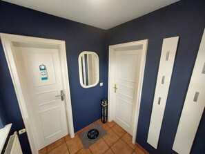 A hallway with two white doors, a small mirror, a black bag, and a doormat.