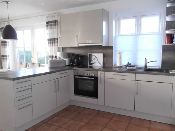 A modern kitchen with white cabinets, a built-in oven, a coffee maker, and a window with blinds.