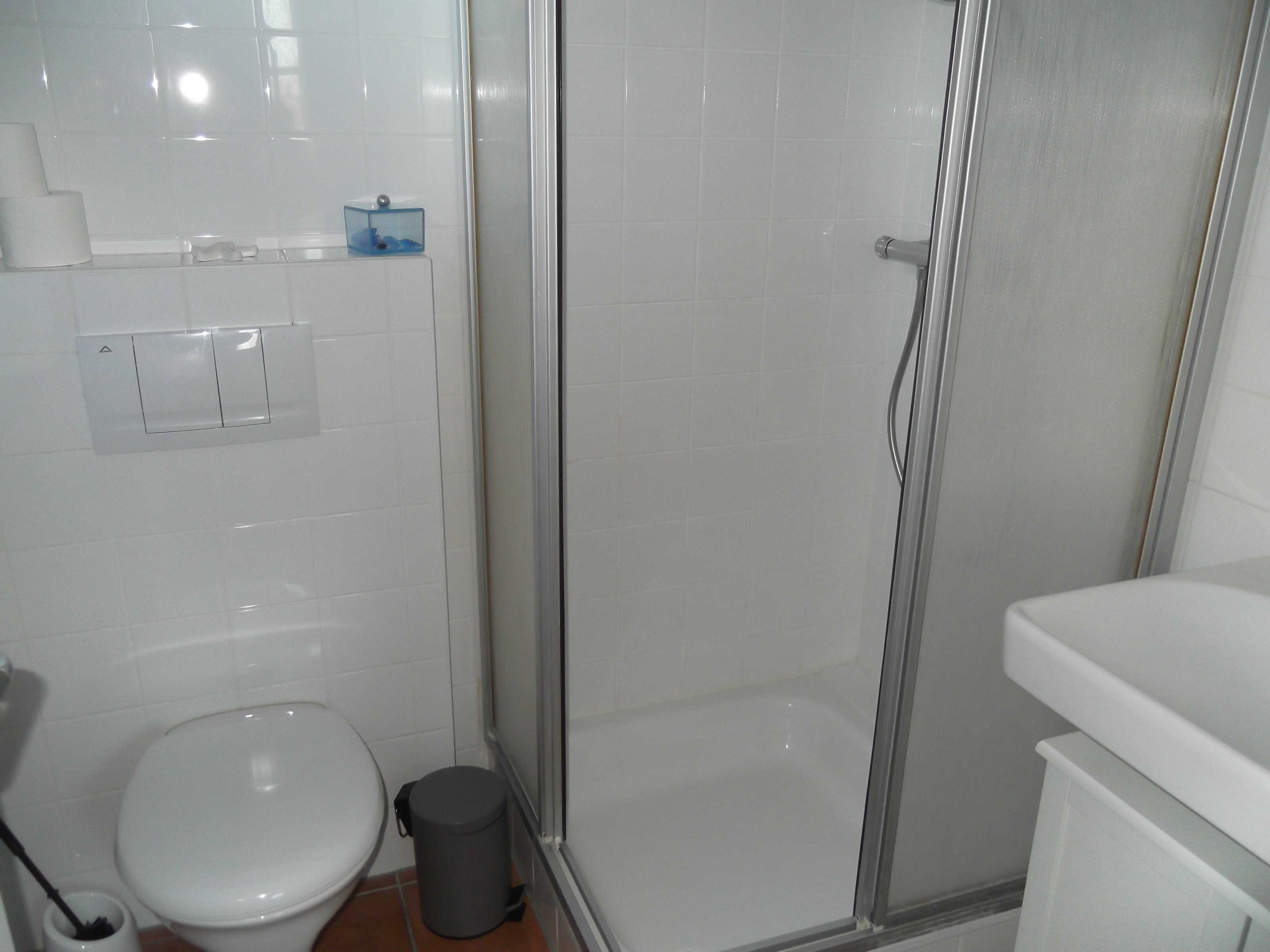 Uma casa de banho com sanita, um cesto de lixo, chuveiro com porta de vidro e lavatório.