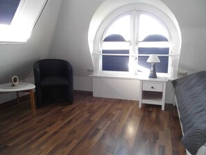 A bedroom with a skylight, a desk with a lamp, a chair, and a bed.
