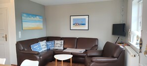 A living room with a brown leather sofa, a small white table, and a TV on a stand.