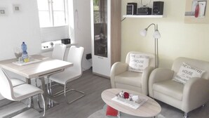 A modern living room with a dining table, two armchairs, a coffee table, and a built-in kitchen cabinet. - Rungholtstr. 3 a, apt. jetsam (Wyk auf Föhr)