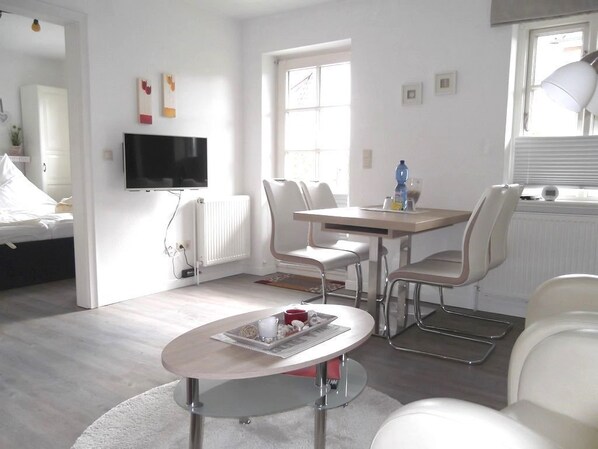 A modern hotel room with a bed, a TV, a dining table with chairs, and a small round table with a tray.
