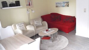 A living room with a red sofa, two white armchairs, a coffee table, and a small table with a lamp. - Rungholtstr. 3 a, apt. jetsam (Wyk auf Föhr)