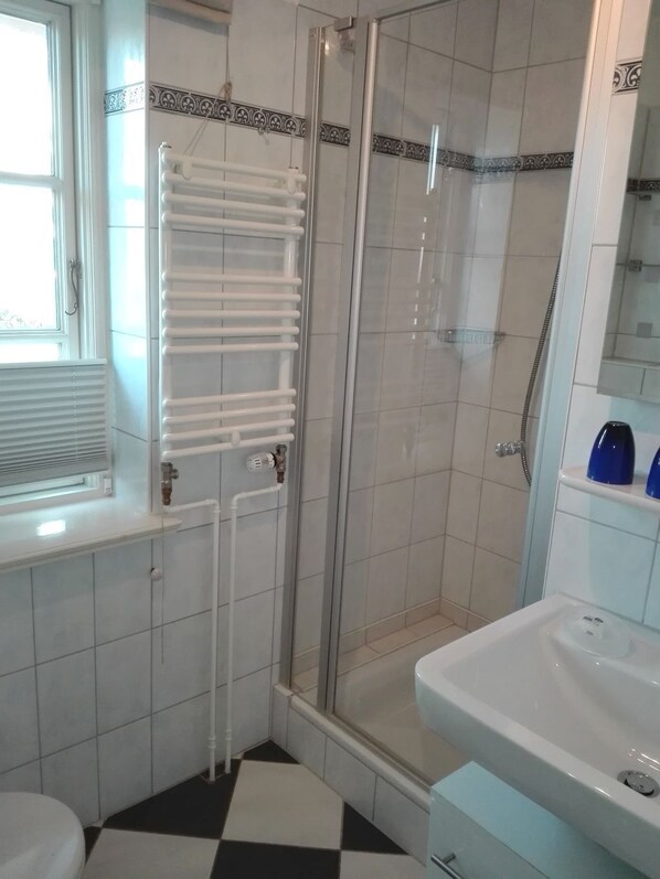 A bathroom with a glass-enclosed shower, a white radiator, a white sink, and a checkered floor.