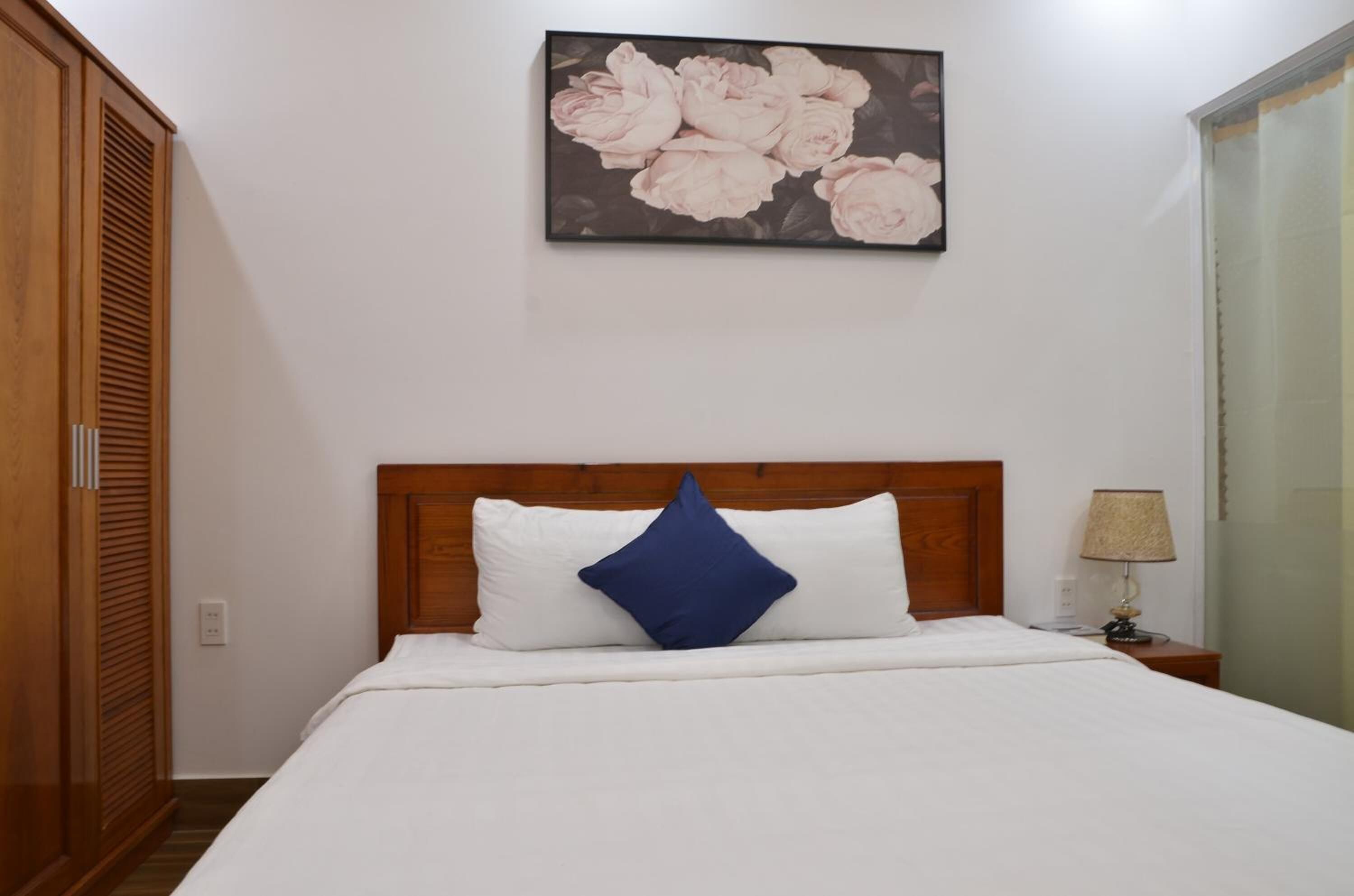 A neatly made bed with a wooden headboard, a blue pillow, and a wall-mounted floral artwork.