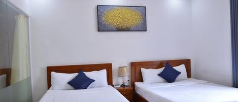 Habitación de hotel con dos camas, una lámpara de techo, una obra de arte en la pared y una mesita de noche con lámpara.