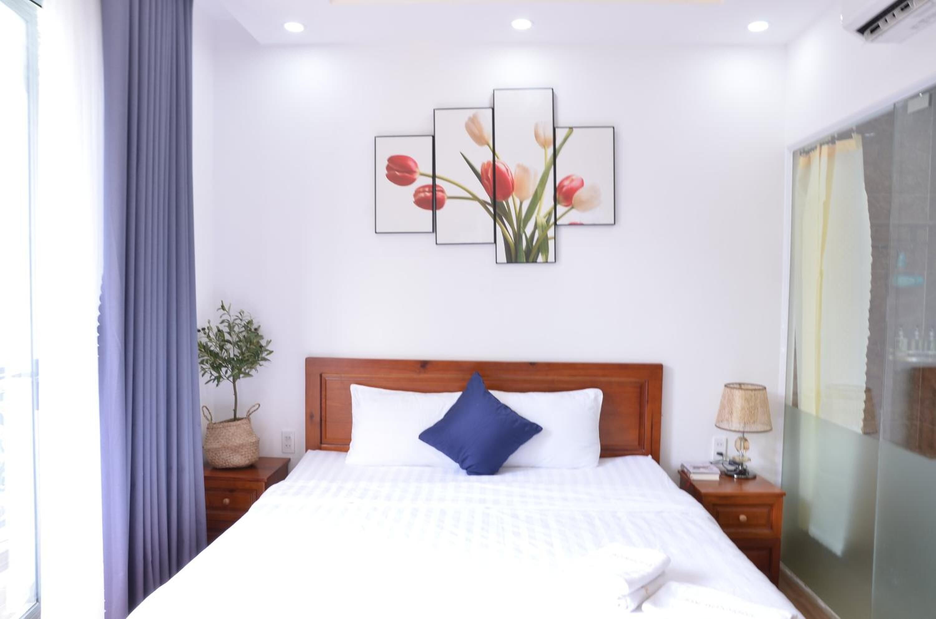 Hotelkamer met een bed, nachtkastje, lamp, raam met gordijnen en een wanddecoratie van tulpen.