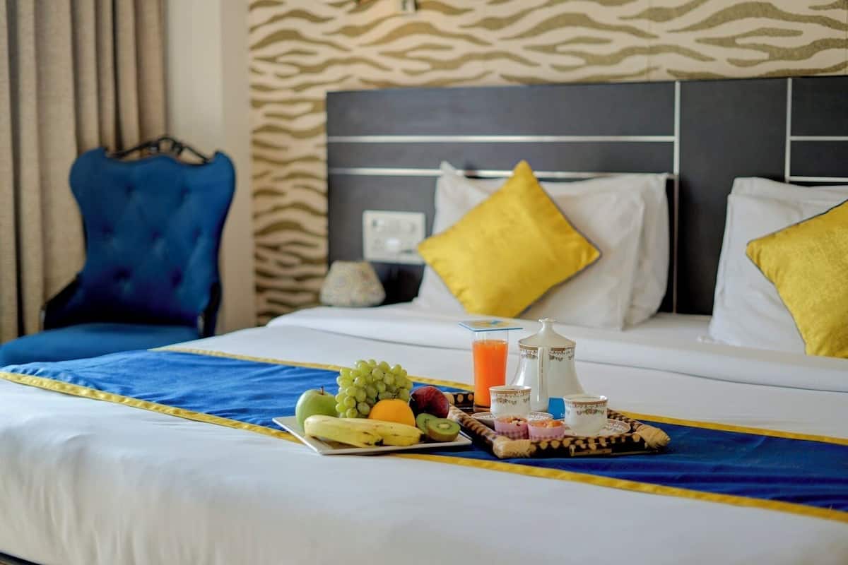A hotel room with a neatly made bed, a tray of fruits and juice, and a breakfast setup.