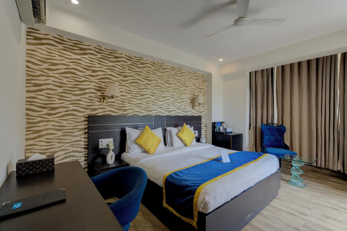 A hotel room with a zebra-patterned wall, a bed with blue and yellow bedding, a desk with a lamp, and a chair.