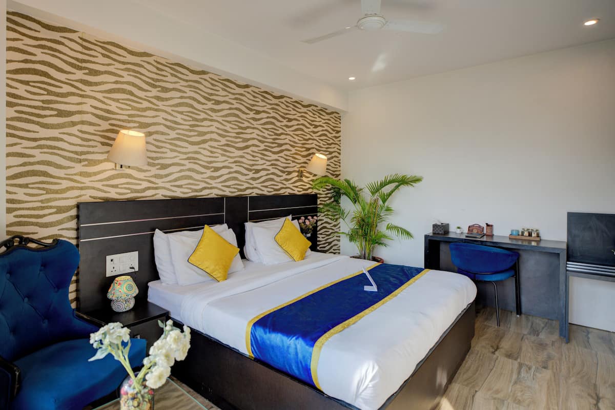 A hotel room with a zebra-patterned wall, a bed with white and yellow bedding, a blue chair, a desk with a computer, and a ceiling fan.