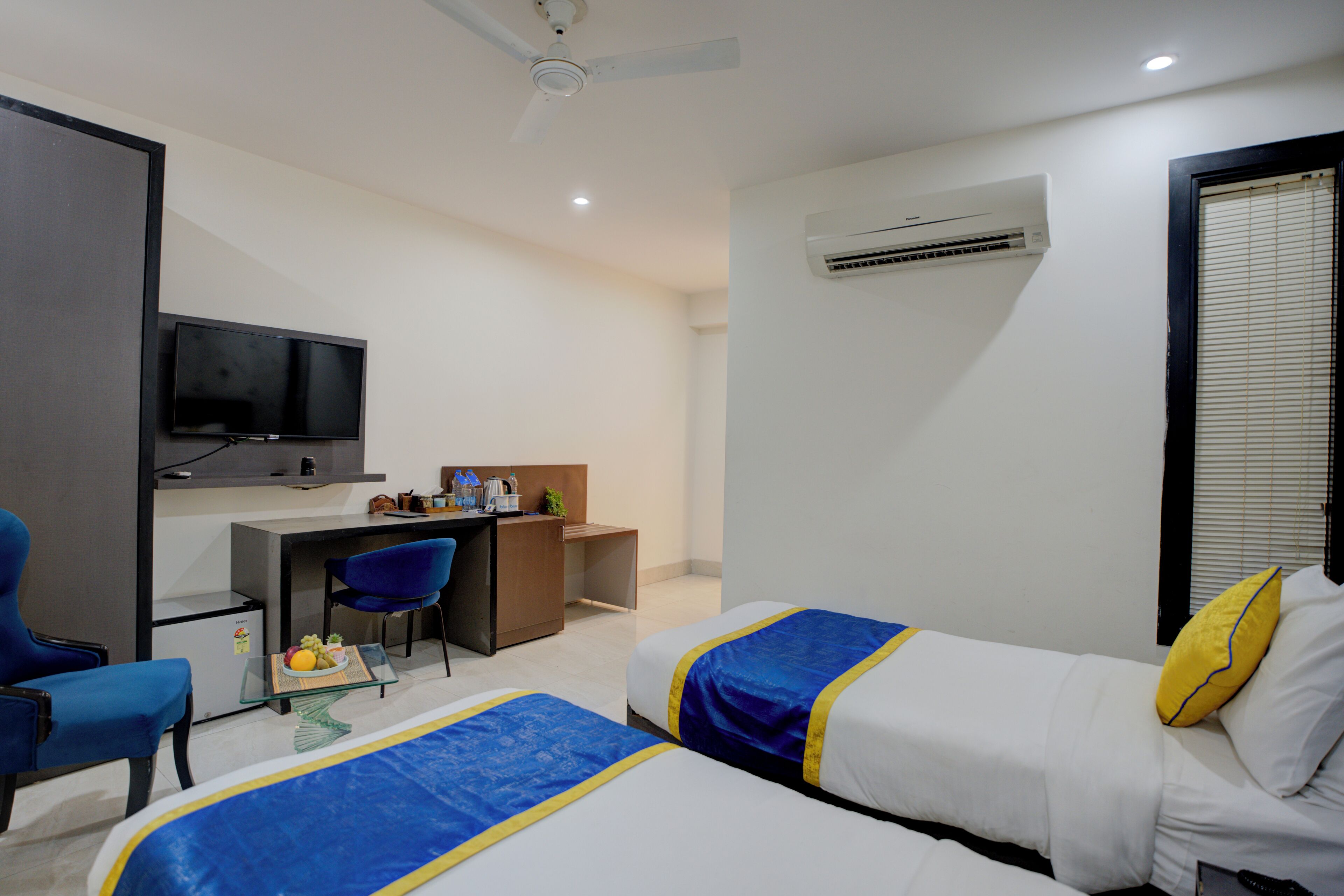 A hotel room with two beds, a desk, a chair, a television, and an air conditioning unit.