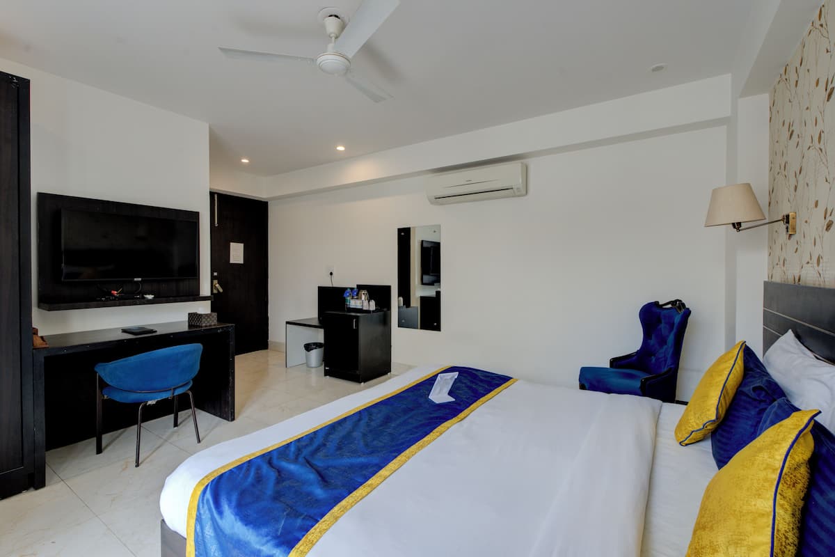 A hotel room with a large bed, a desk, a chair, a television, and a ceiling fan.