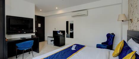 Quarto de hotel com uma cama grande, uma escrivaninha, uma cadeira, uma televisão e um ventilador de teto.