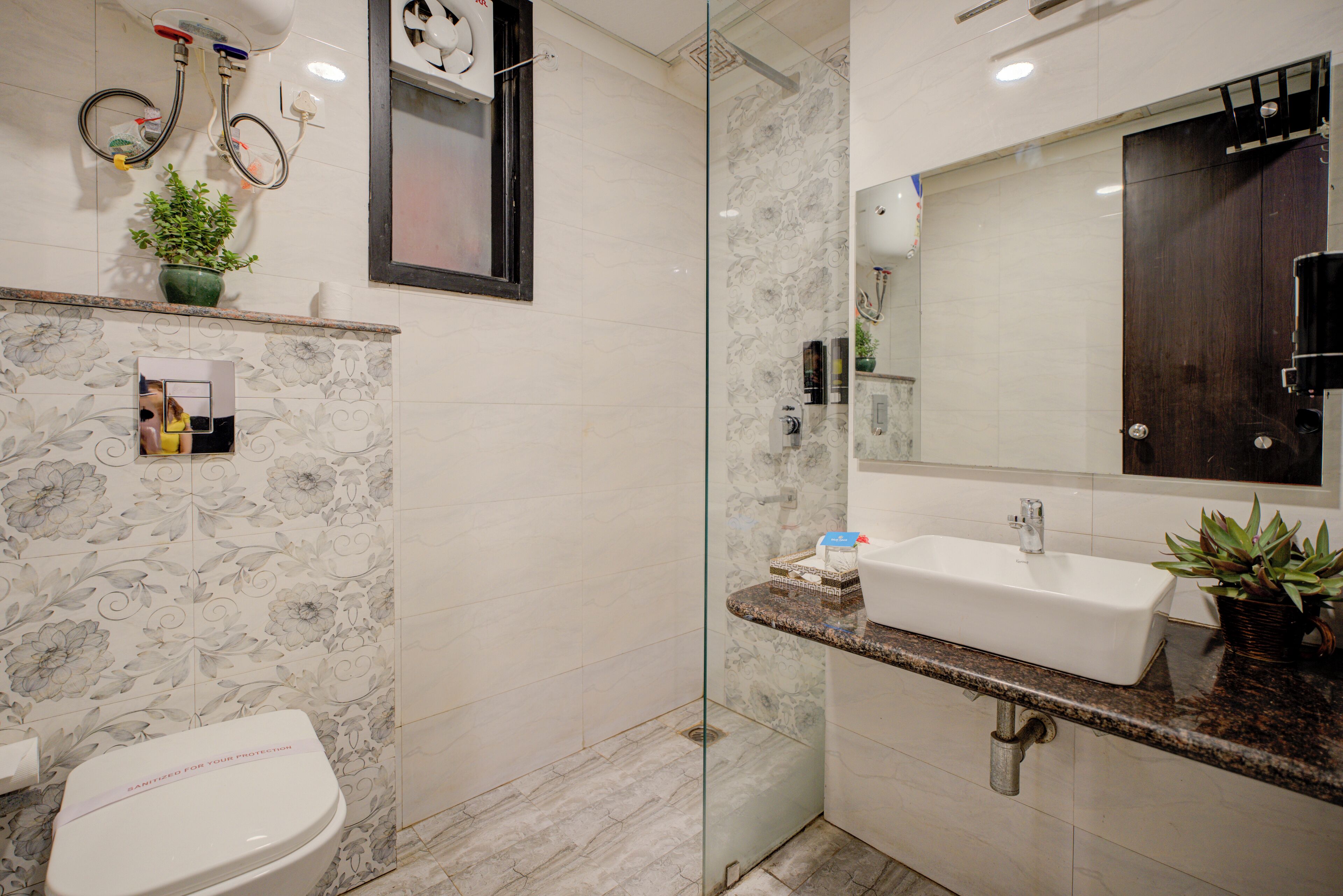 A modern bathroom with a toilet, a glass shower enclosure, a sink with a marble countertop, and a large mirror.