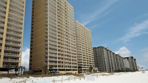 Ett högt hotell med flera balkonger, en sandstrand i förgrunden och klarblå himmel.
