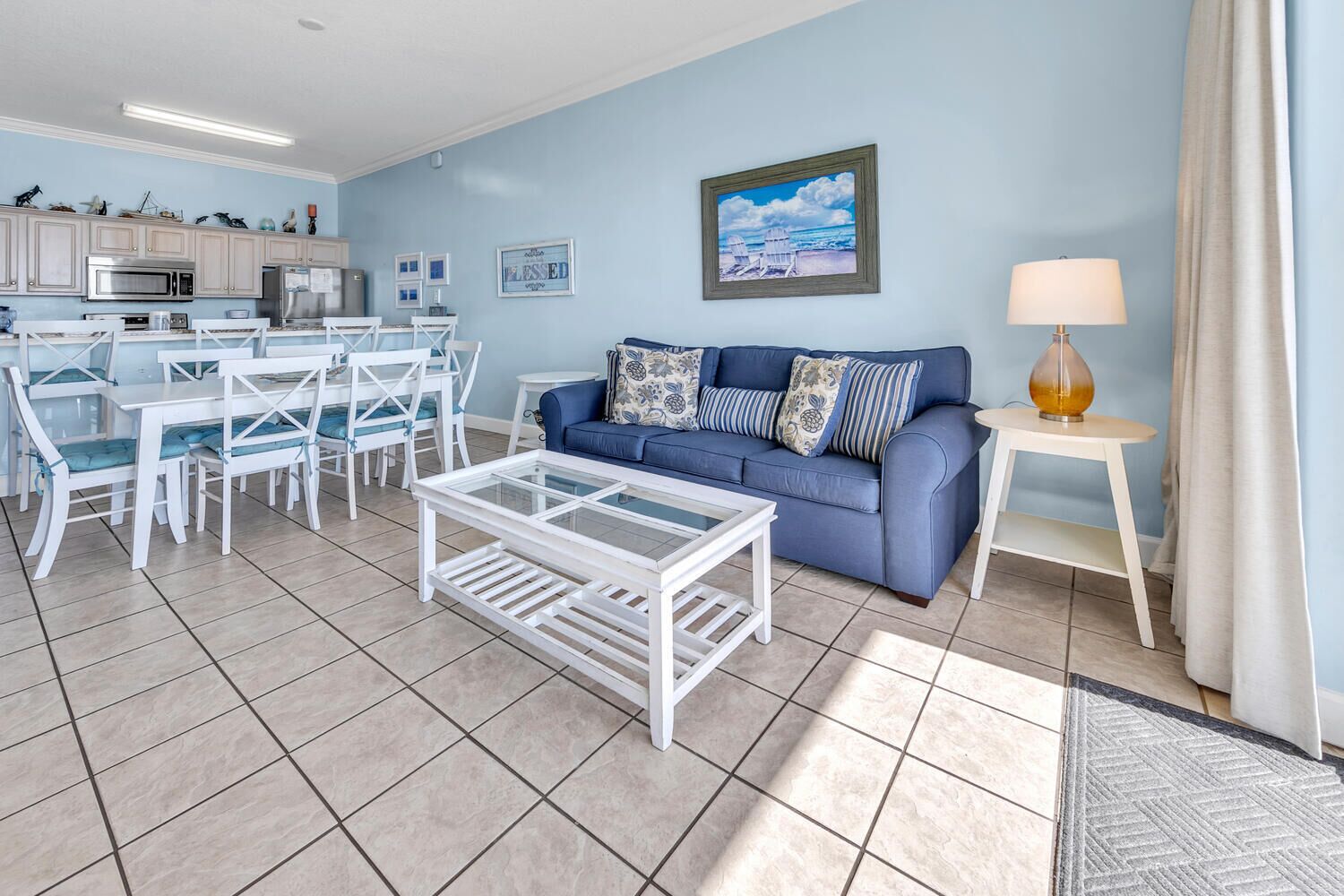 Un salon avec un canapé bleu, une table basse blanche et un coin repas avec des chaises blanches.